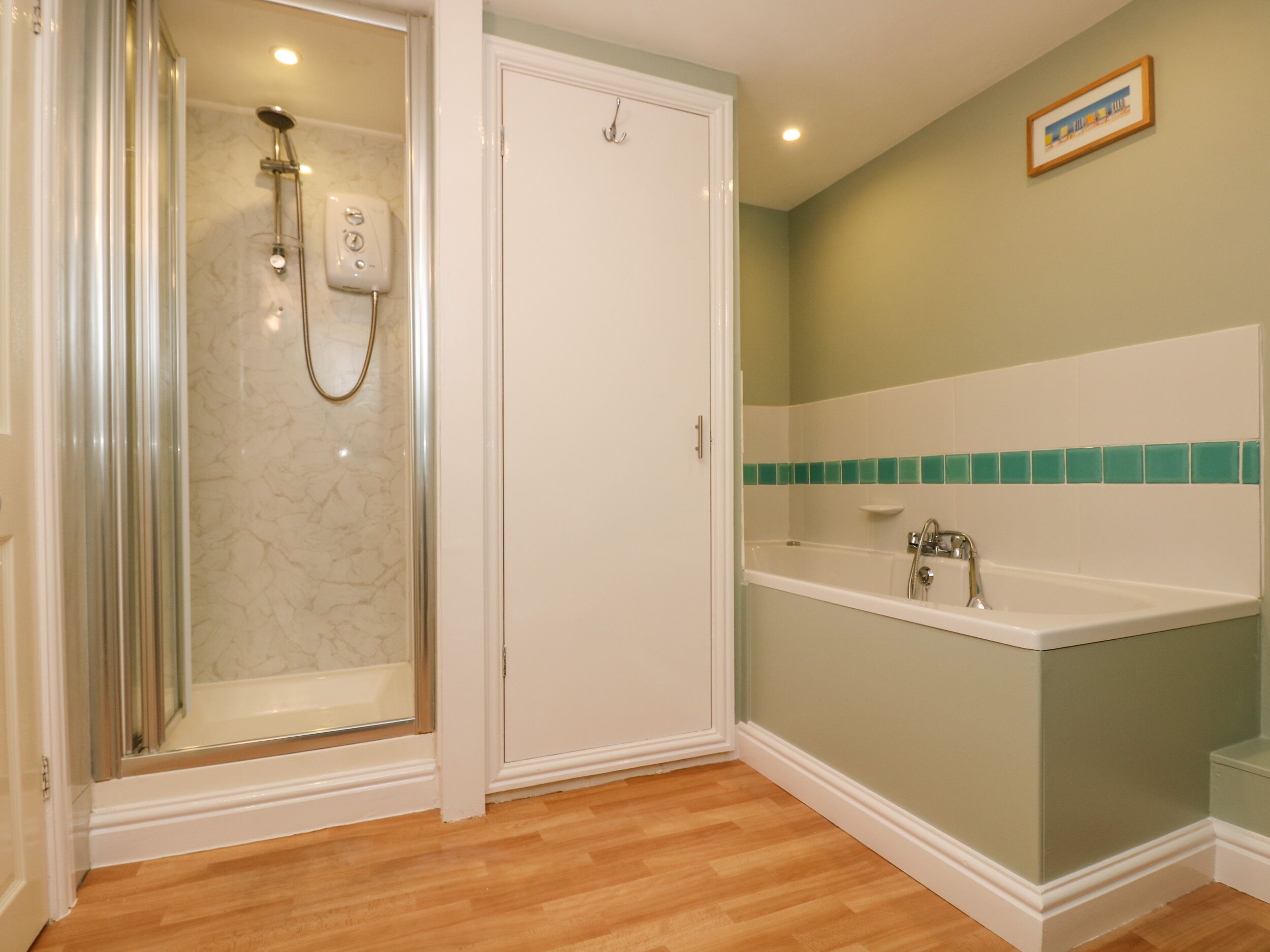 A bathroom with a glass-enclosed shower, a white bathtub, and a sink with a green-tiled backsplash.