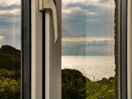 Vista a través de una ventana de marco blanco, que muestra una masa de agua, vegetación y un cielo nublado.