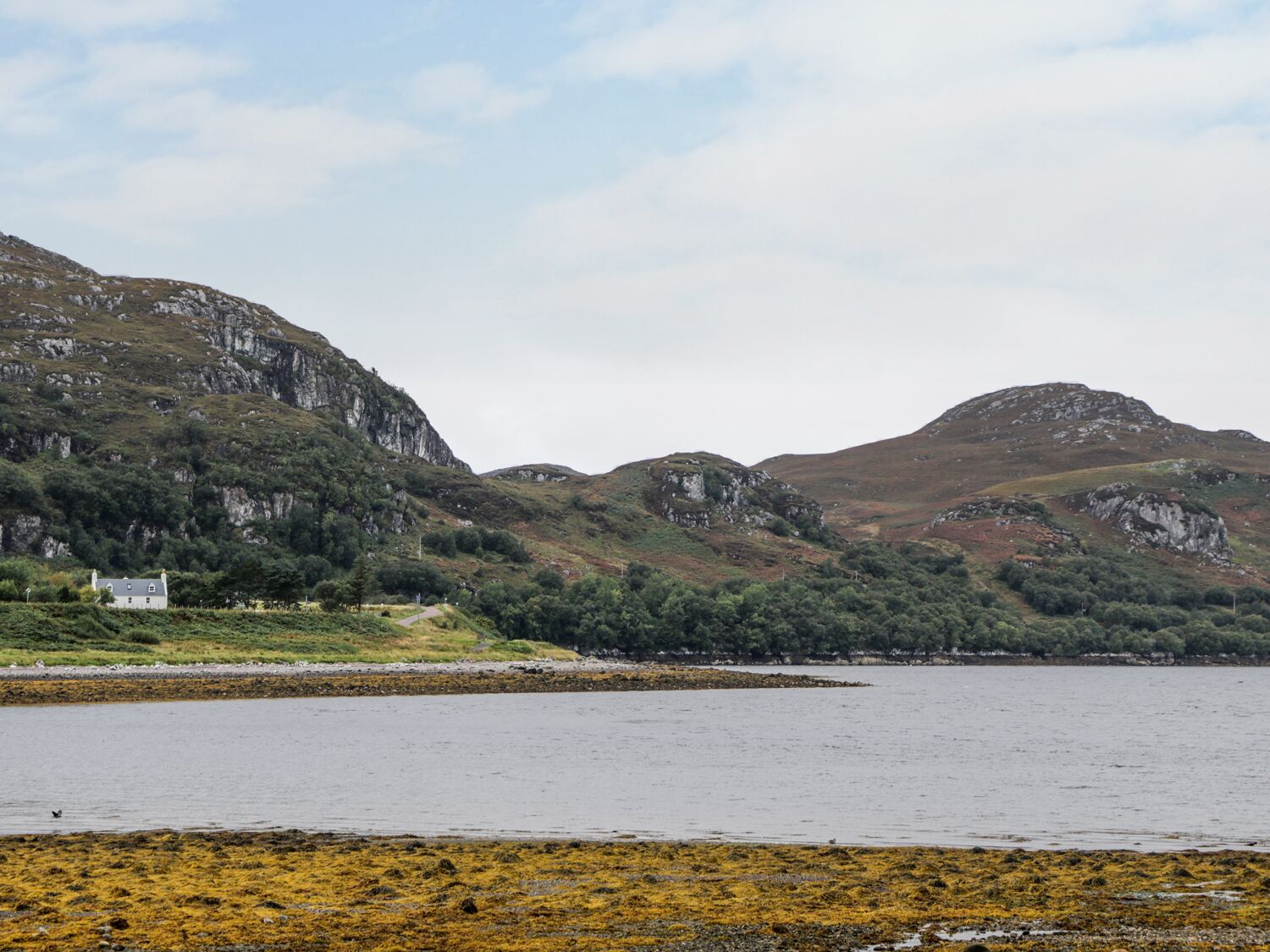 A coastal landscape with rocky hills, a body of water, and a small building.