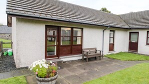 A single-story house with a tiled roof, a front door, and a small patio area with a bench and a flower pot. - Church House (Achnasheen)
