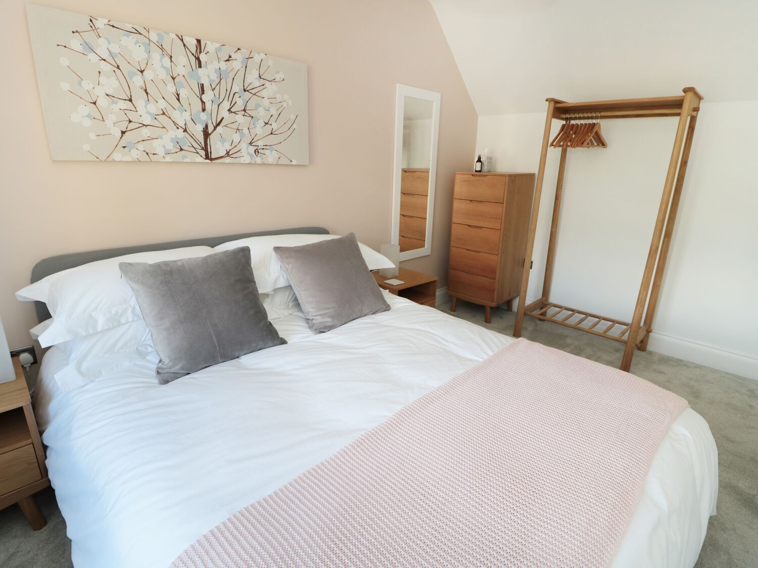 A bedroom with a bed, a dresser, a wardrobe, a wooden drying rack, and a wall-mounted mirror.