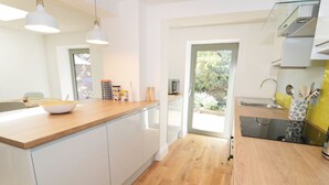 Una cocina moderna con armarios blancos, encimera de madera y una puerta de vidrio que da a un jardín.