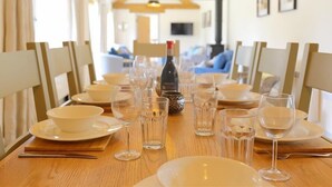 Une table à manger dressée avec de l’assiette blanche, des bols et des verres à vin, et une bouteille de vin placée au centre.