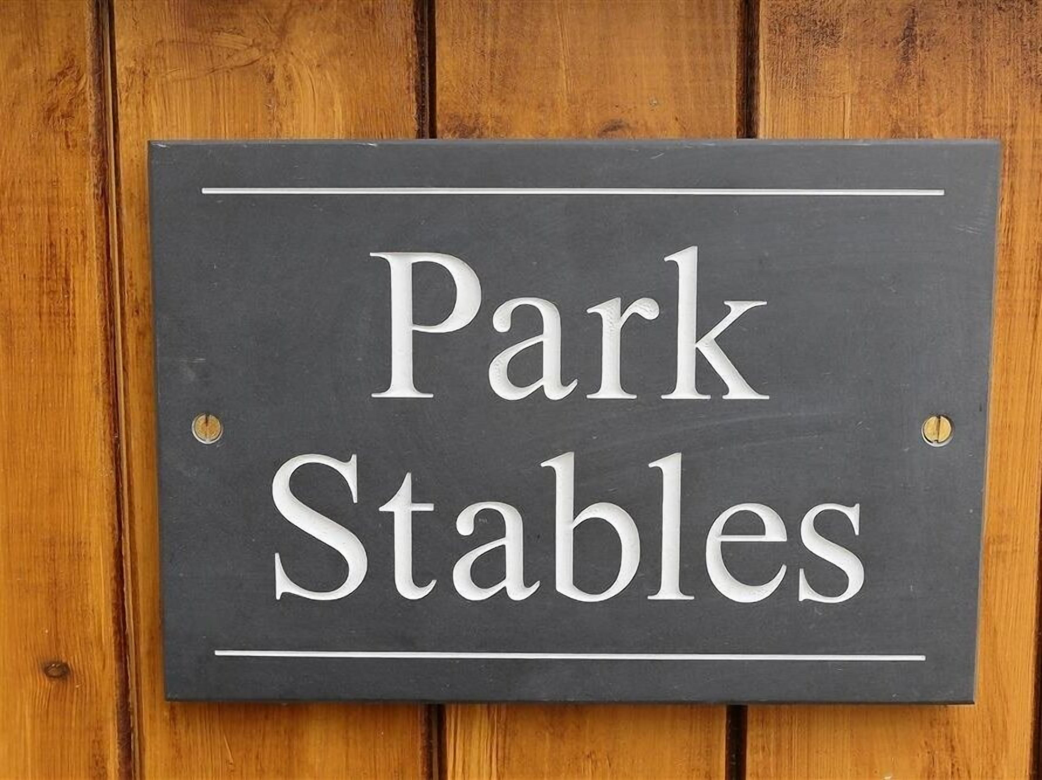 A sign with the text "Park Stables" mounted on a wooden background.