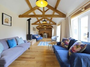 A spacious living room with wooden beams, a fireplace, and a large window.