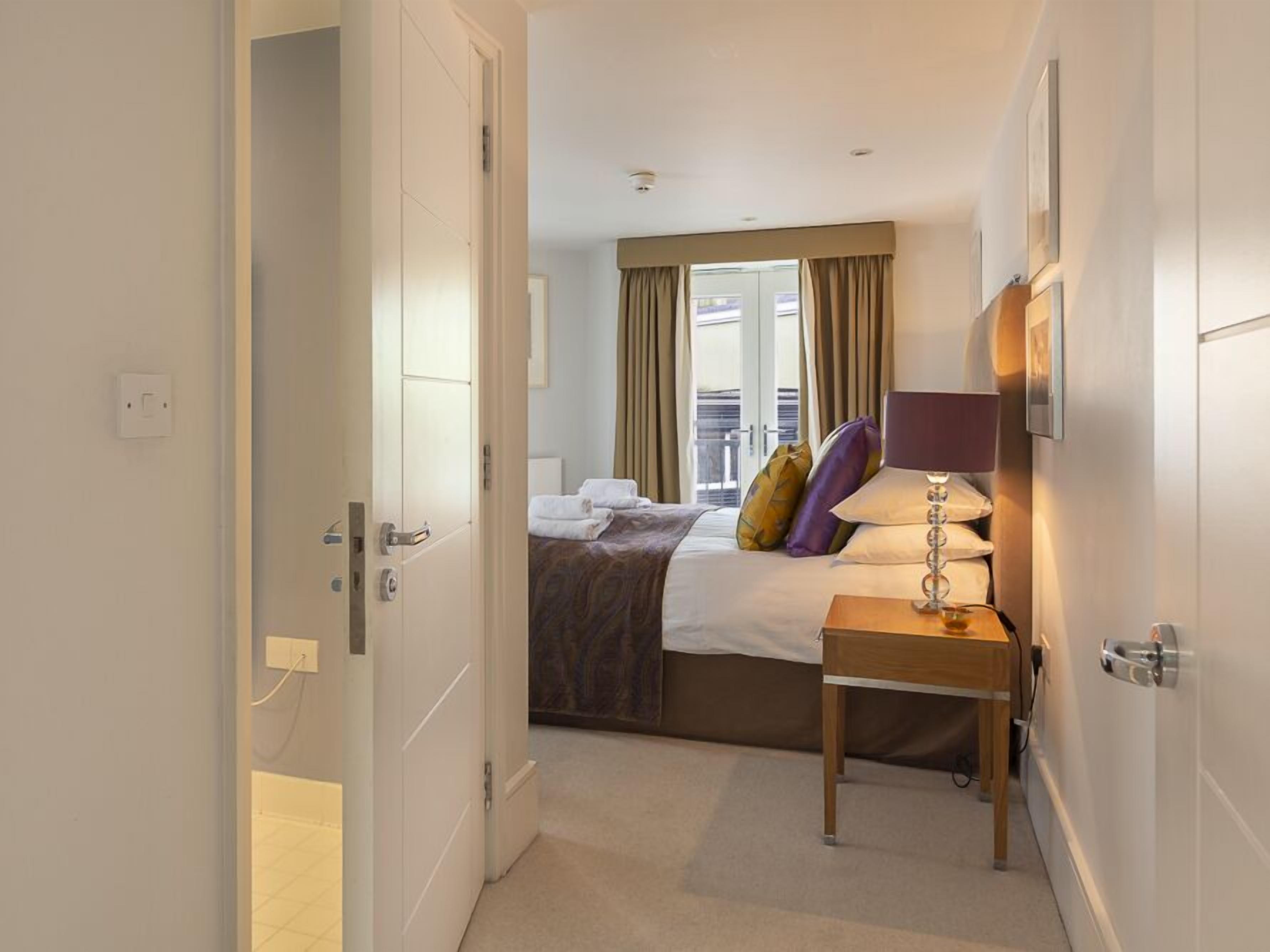 A hotel room with a bed, a bedside table with a lamp, and a window with curtains.