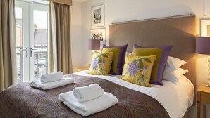 A hotel room with a large bed, two pillows with floral patterns, a headboard, a bedside table with a lamp, and a view through a sliding door to the outside. - 44 Dart Marina (Dartmouth)