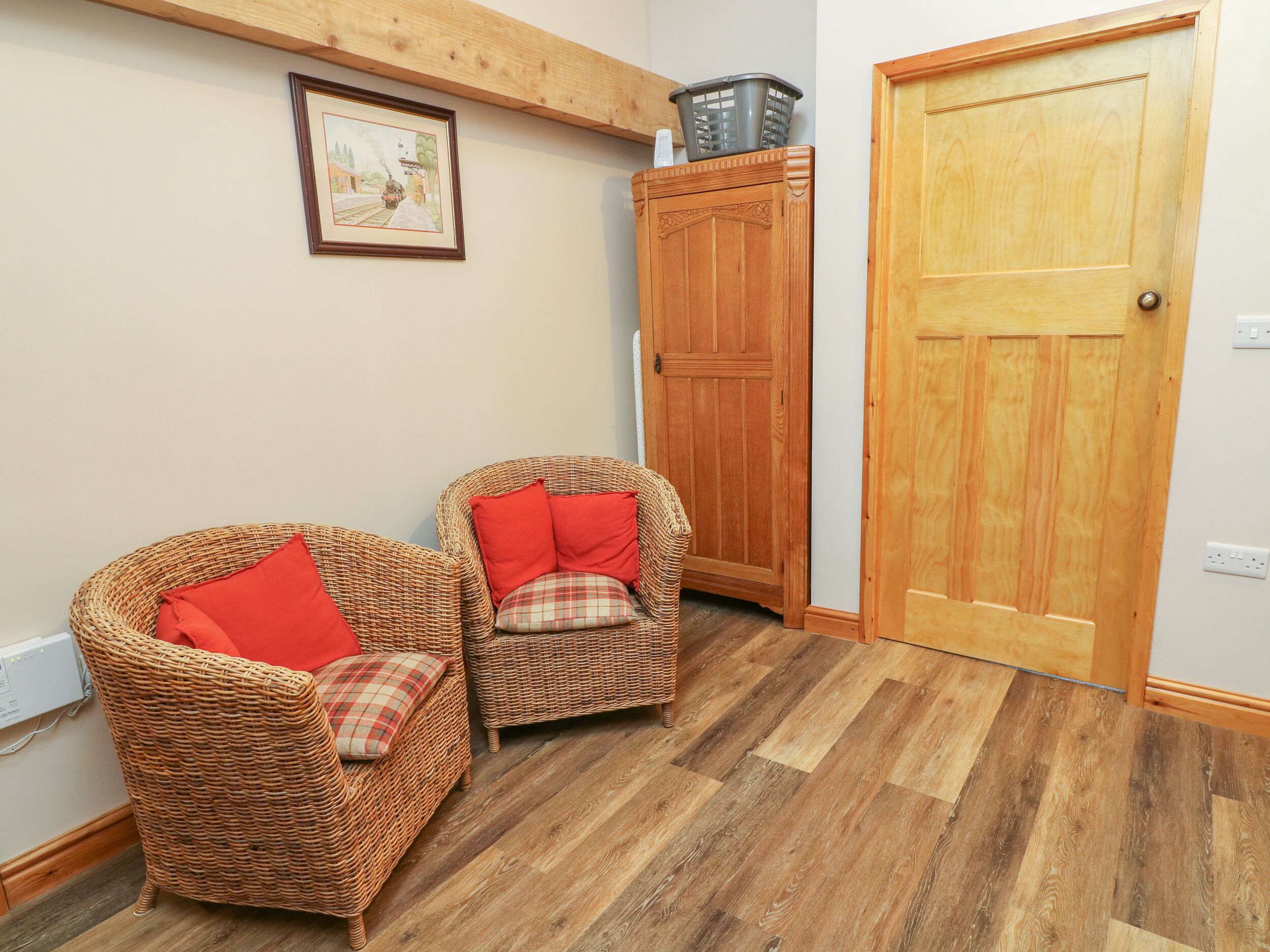 A room with two wicker chairs with red and plaid cushions, a wooden cabinet, and a wooden door.