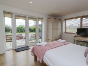 A bedroom with a bed, a TV, a wardrobe, and a sliding glass door leading to an outdoor patio area. - Coney Garth Retreat (Beckermet)