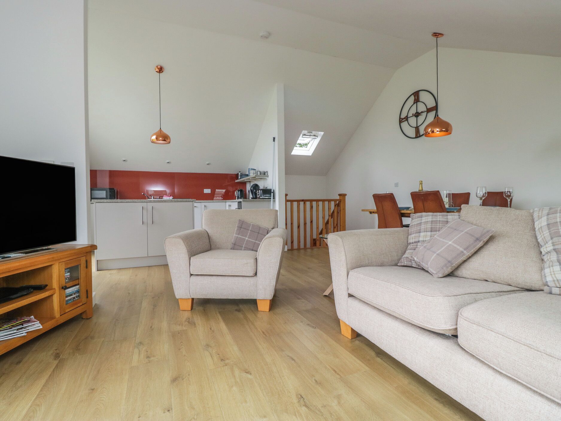 A living room with a television, two sofas, a wooden entertainment unit, and a kitchen in the background.