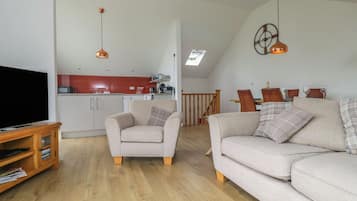 A living room with a television, two sofas, a wooden entertainment unit, and a kitchen in the background.