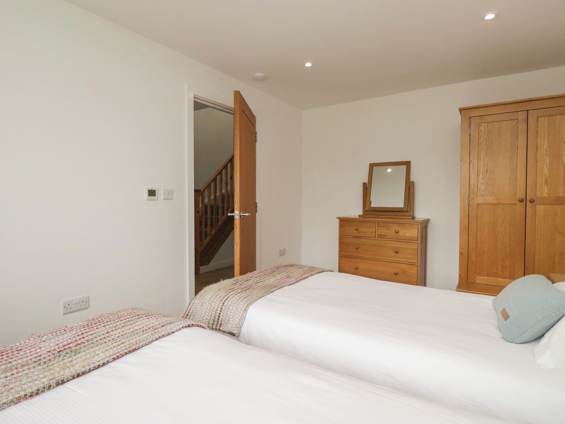 A bedroom with two beds, a wooden wardrobe, a dresser, and a mirror.