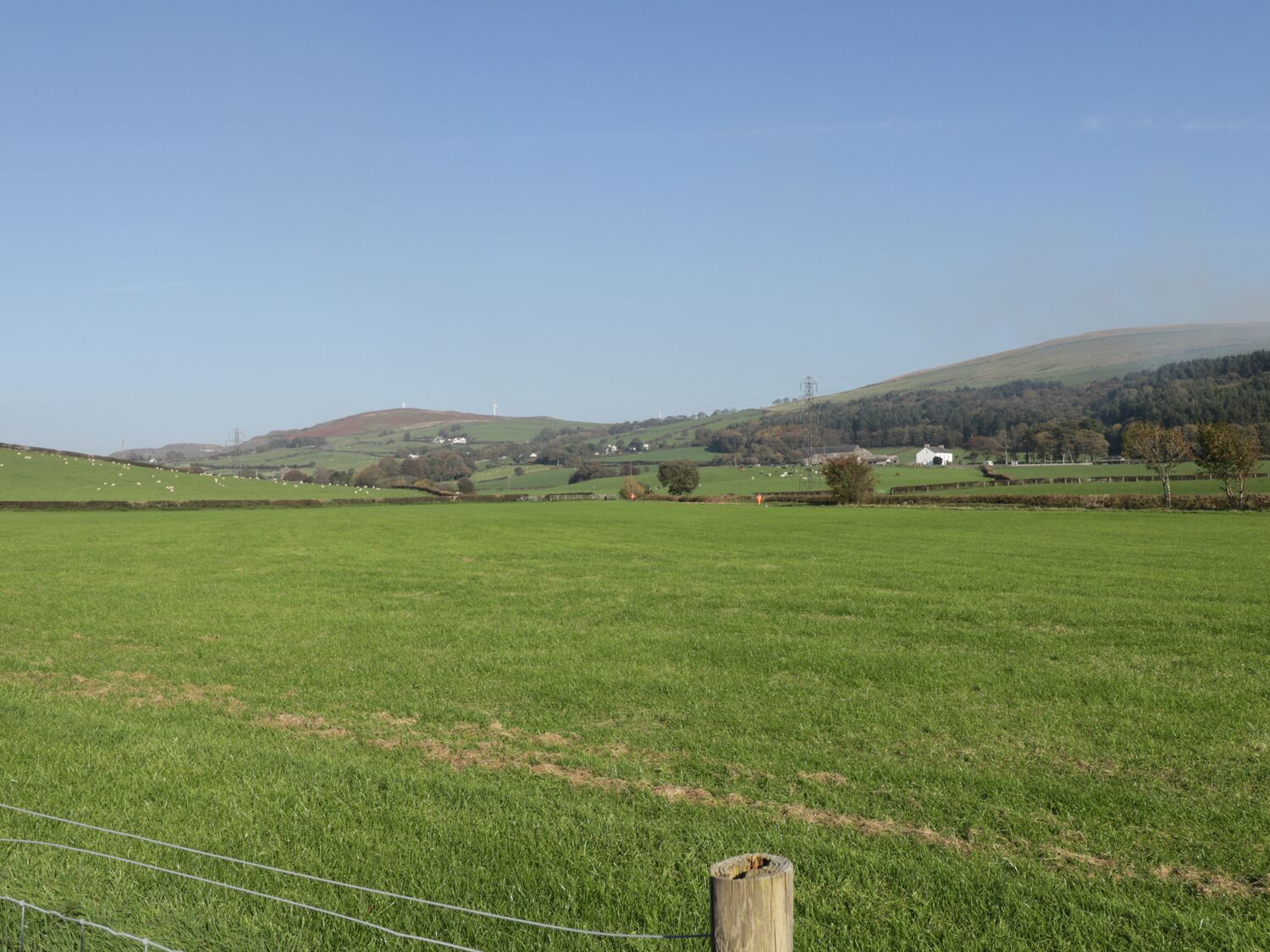 A rural landscape with a large open field, a wooden post, and distant hills.