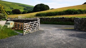 A rural landscape with a gravel driveway leading to a stone wall and a wooden gate. - Yew Fold (Kirkby-in-Furness)