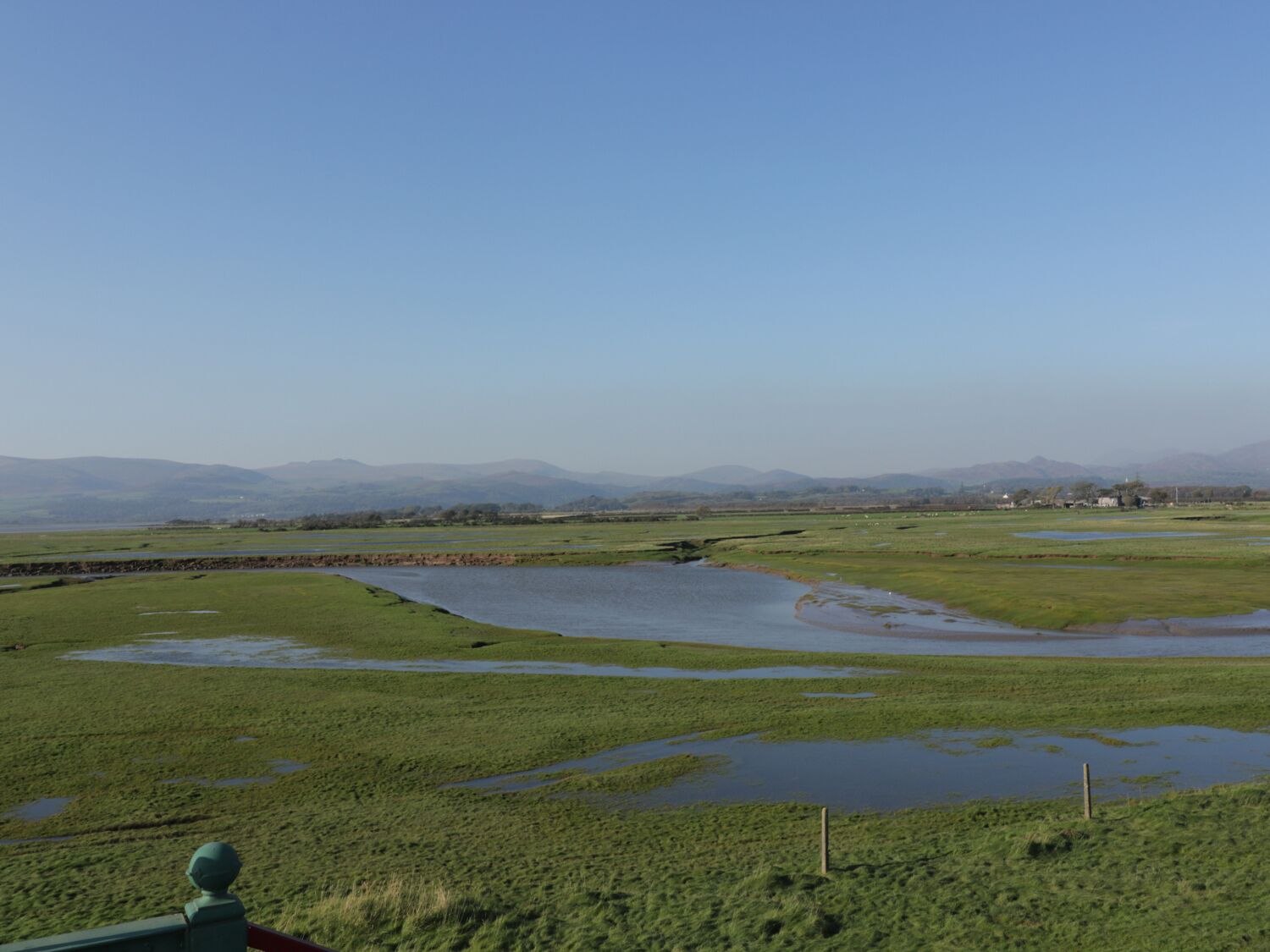 A rural landscape with a river, green fields, and distant mountains.