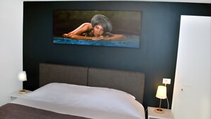 Een slaapkamer met een bed, nachtkastje, een aan de muur bevestigde televisie en een bedlamp.