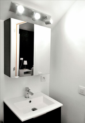 Une salle de bain avec un lavabo blanc, un miroir et un luminaire fixé au mur.