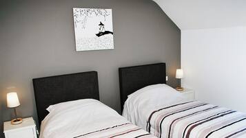 A bedroom with two single beds, each with a dark headboard and white bedding with striped patterns. There are bedside tables with lamps and a wall-mounted artwork above the beds.
