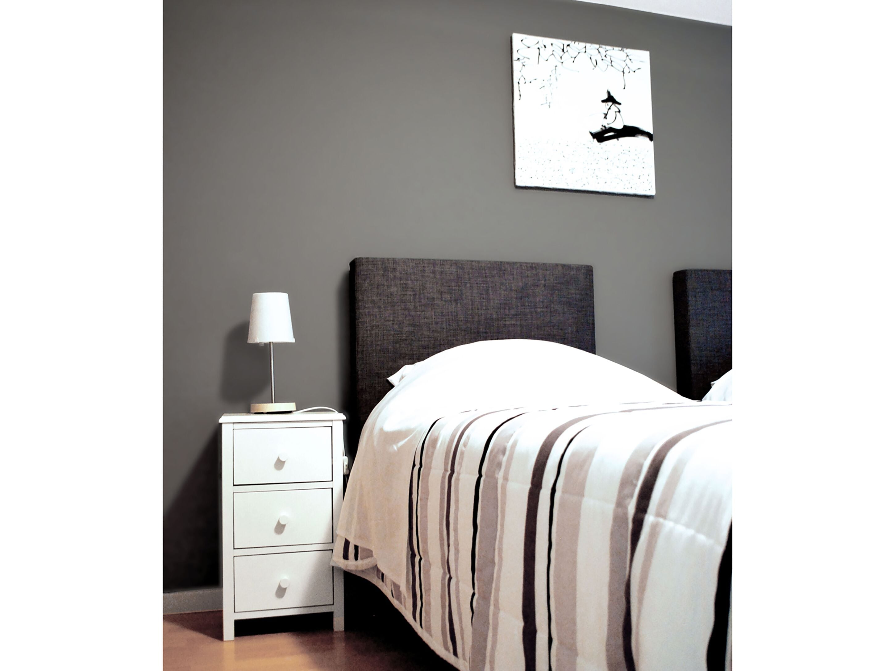 A bedroom with a bed, a nightstand with a lamp, and a wall-mounted artwork.