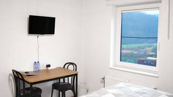 Een kamer met een bed, een bureau met twee stoelen, een aan de muur bevestigde televisie en een raam met uitzicht op een landschap.