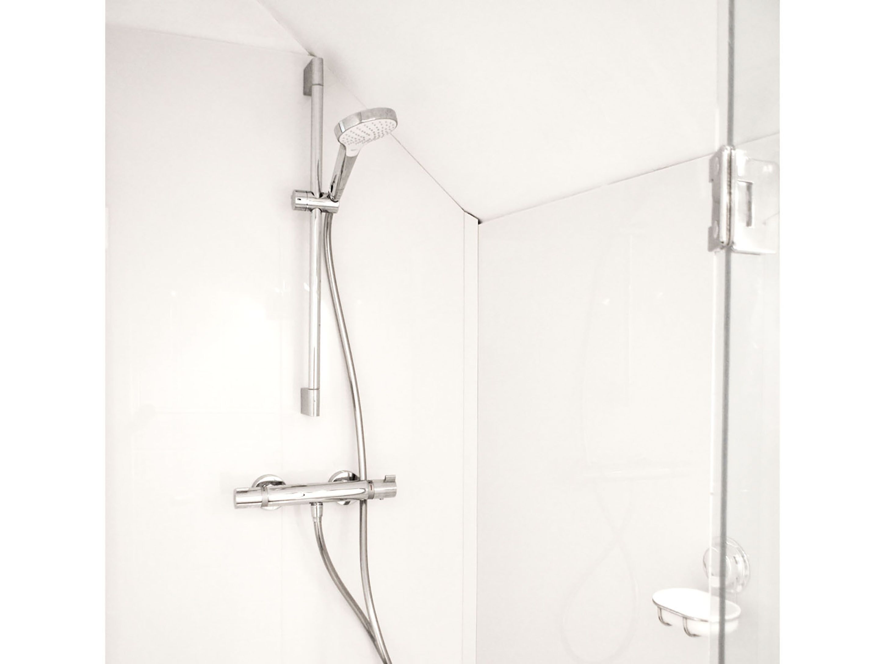 A shower with a handheld showerhead and a wall-mounted control panel.