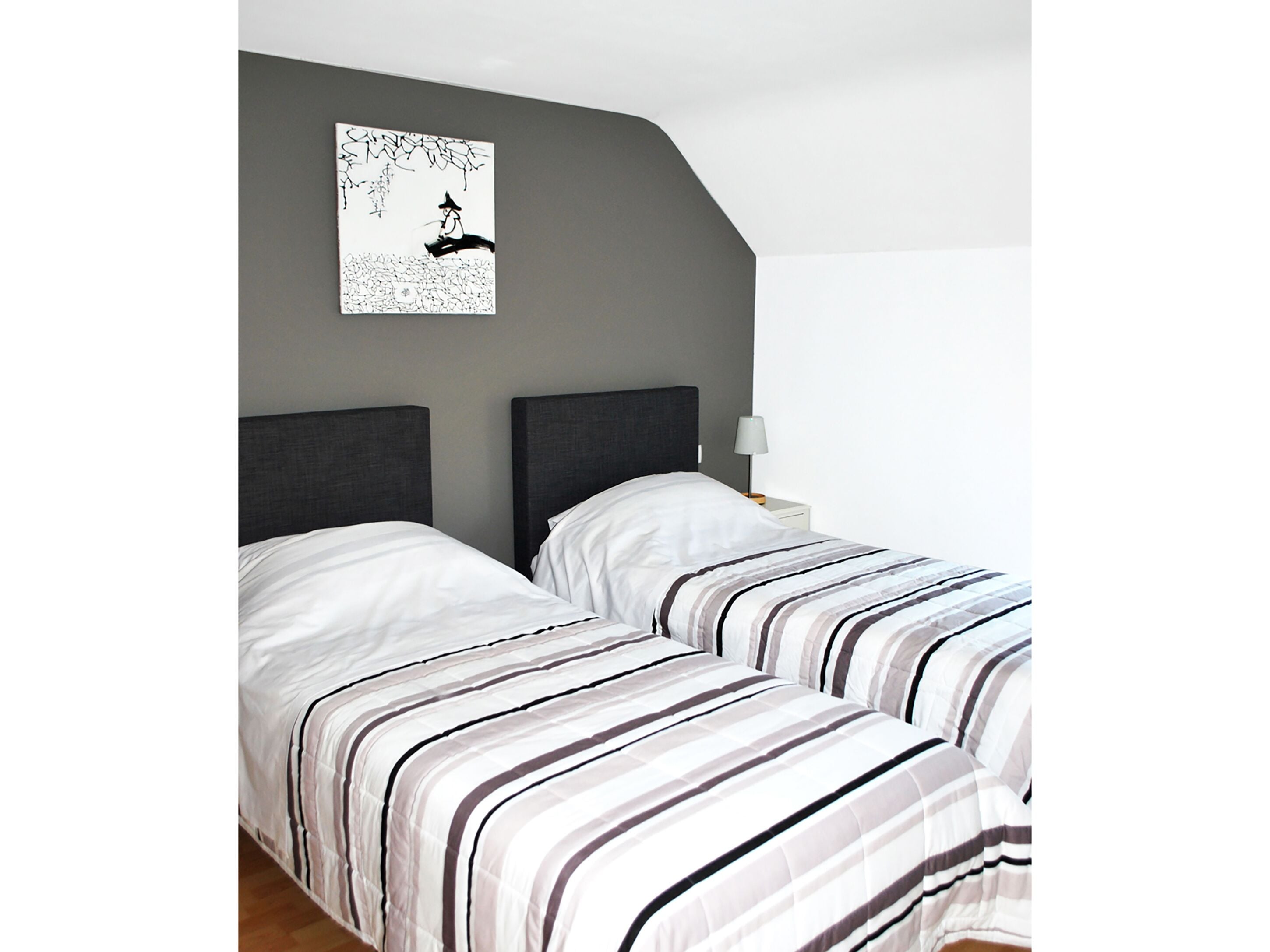 A bedroom with two beds, grey walls, and a framed artwork above the beds.