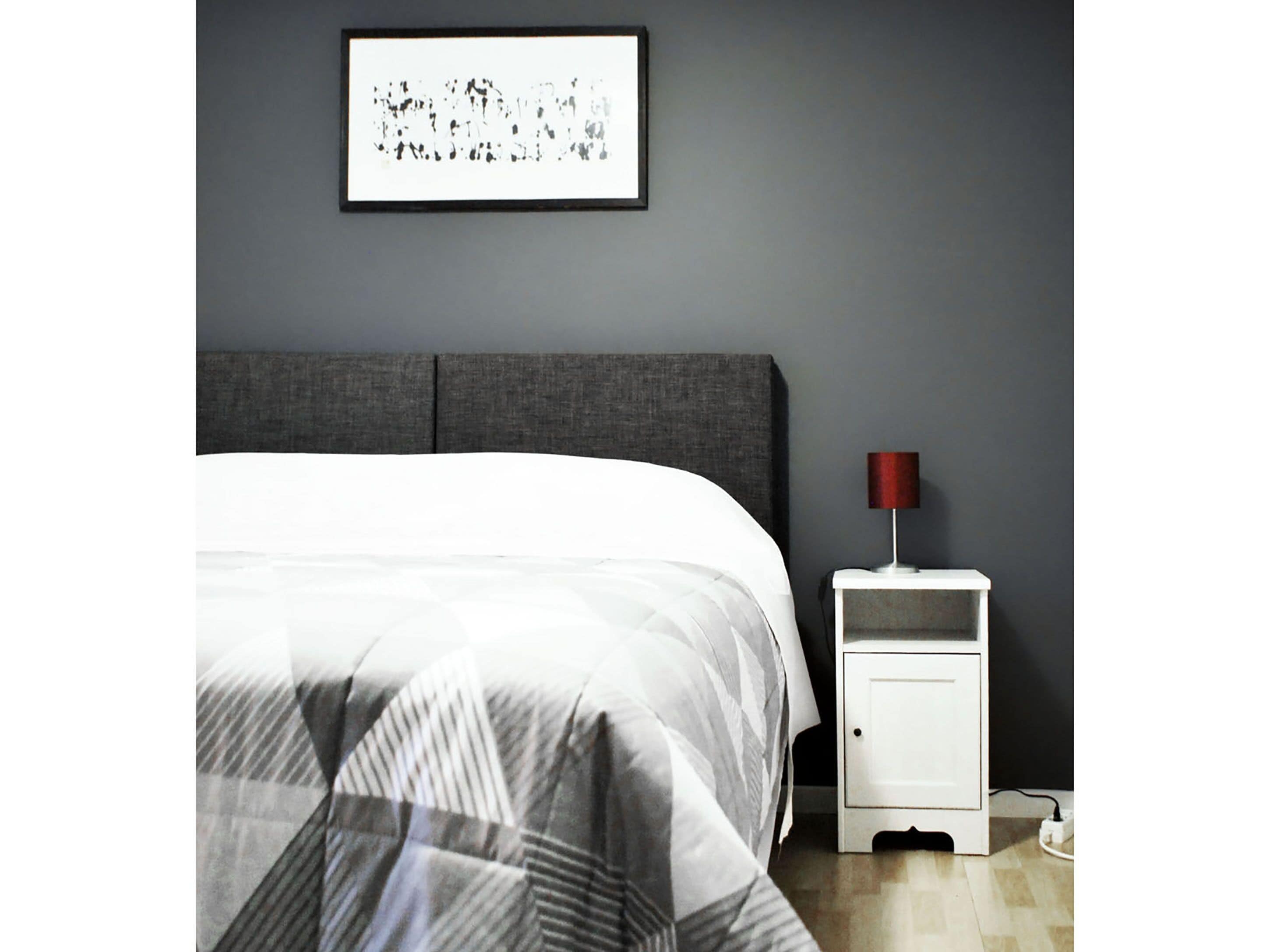 Un dormitorio con cama, mesita de noche, lámpara y un cuadro en la pared.