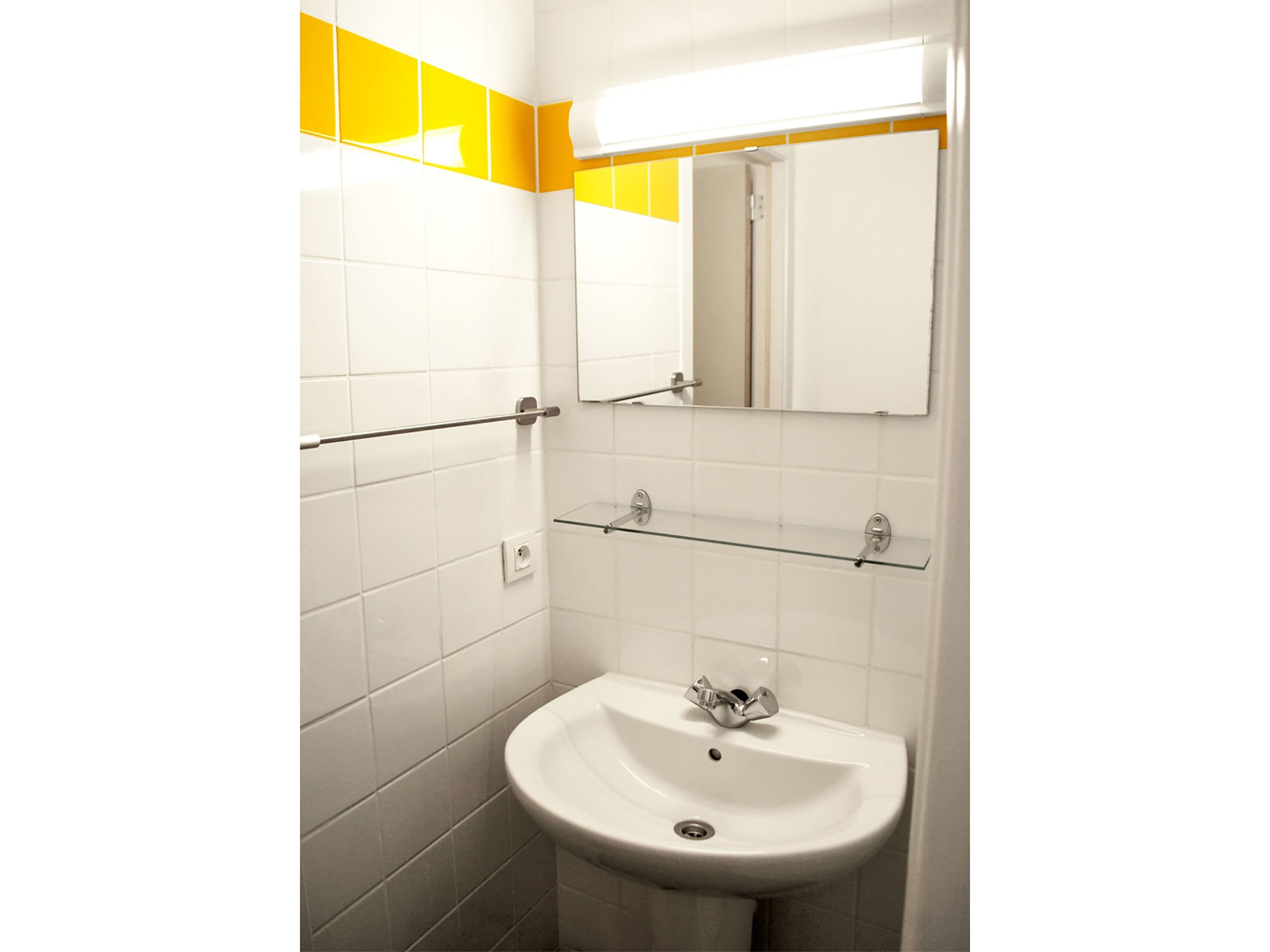 Une salle de bain avec des carreaux blancs, un lavabo, un miroir et un porte-serviettes.