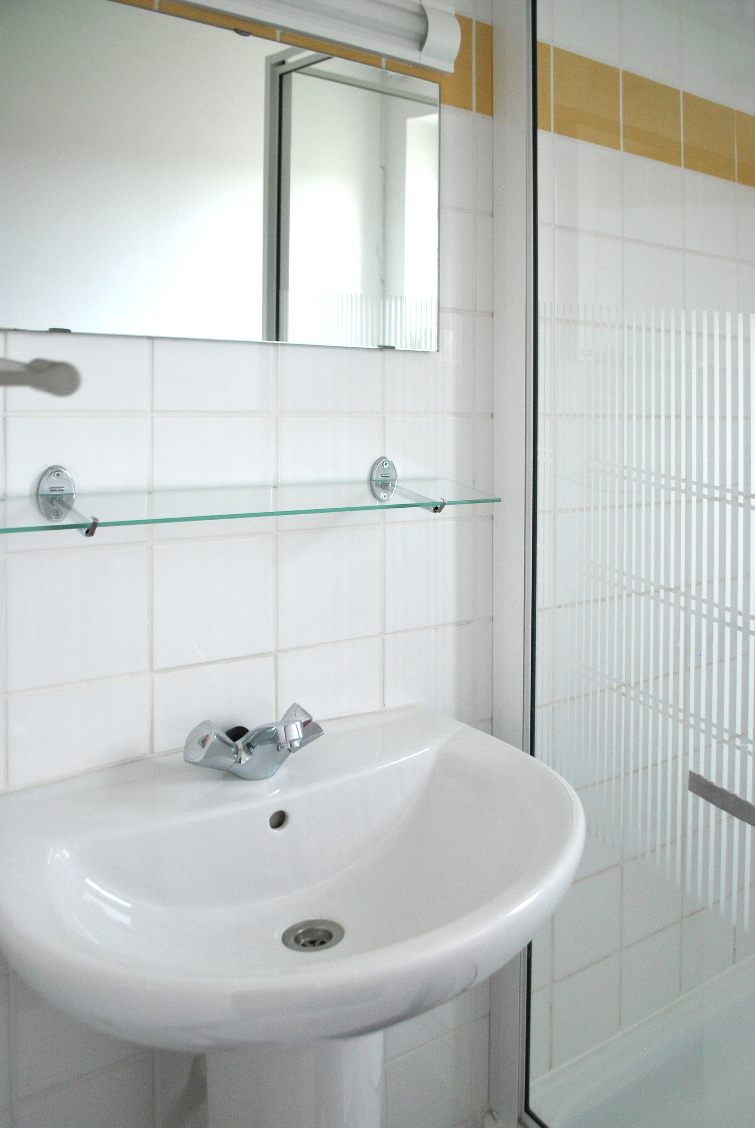 Un bany amb un lavabo blanc, una petita estant de vidre i un mirall damunt del lavabo.