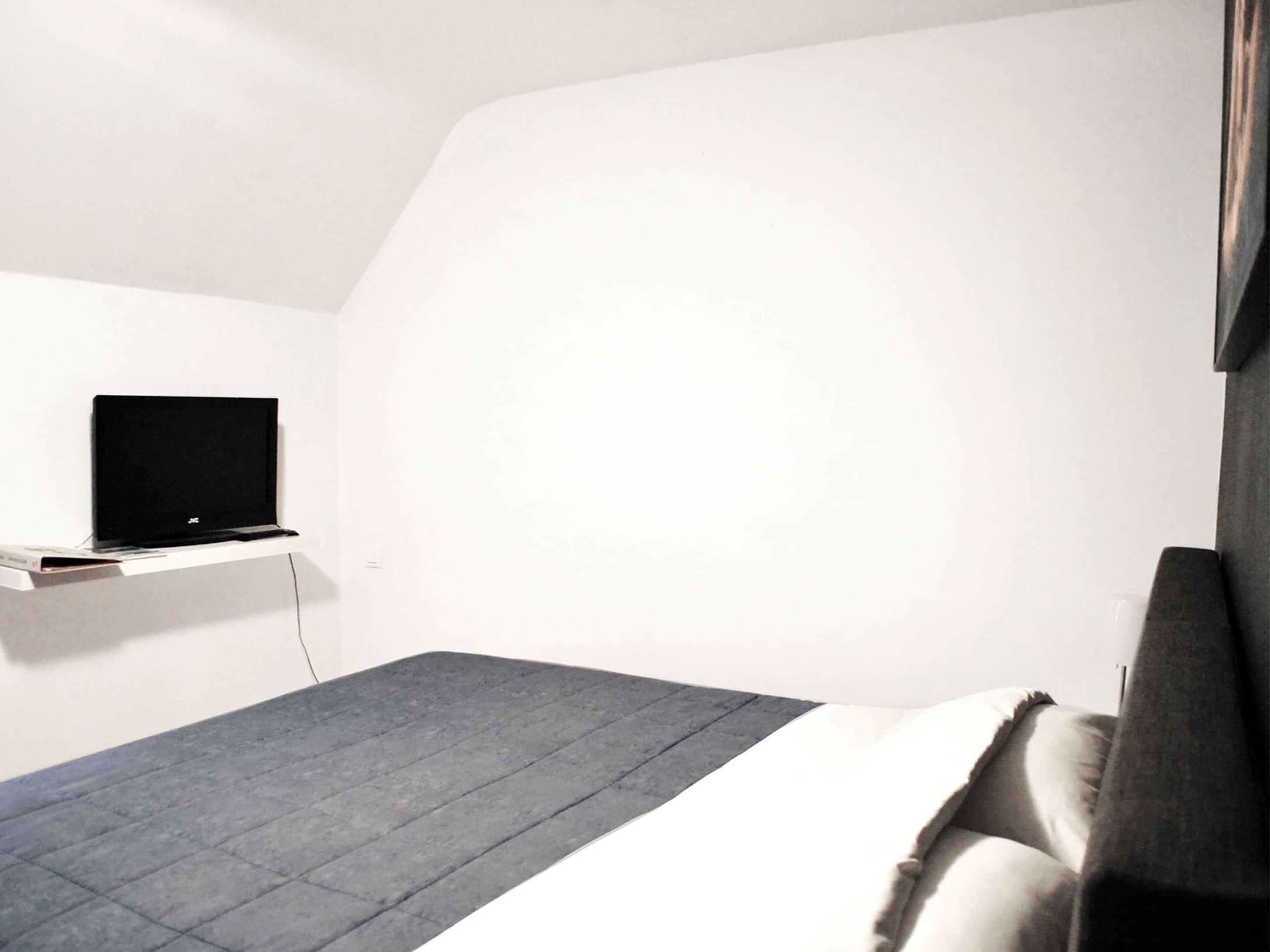 Una camera da letto moderna e accogliente, con un letto, una TV a parete e un arredamento essenziale e ordinato.