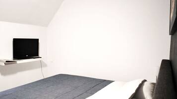 Una camera da letto moderna e accogliente, con un letto, una TV a parete e un arredamento essenziale e ordinato.