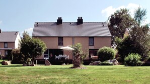 Een herenhuis met twee verdiepingen, een pannendak, een terras met tuinmeubilair en een verzorgd gazon.