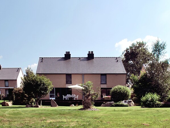 Une maison à deux étages avec un toit en tuiles, une terrasse dotée de mobilier d’extérieur et une pelouse bien entretenue.