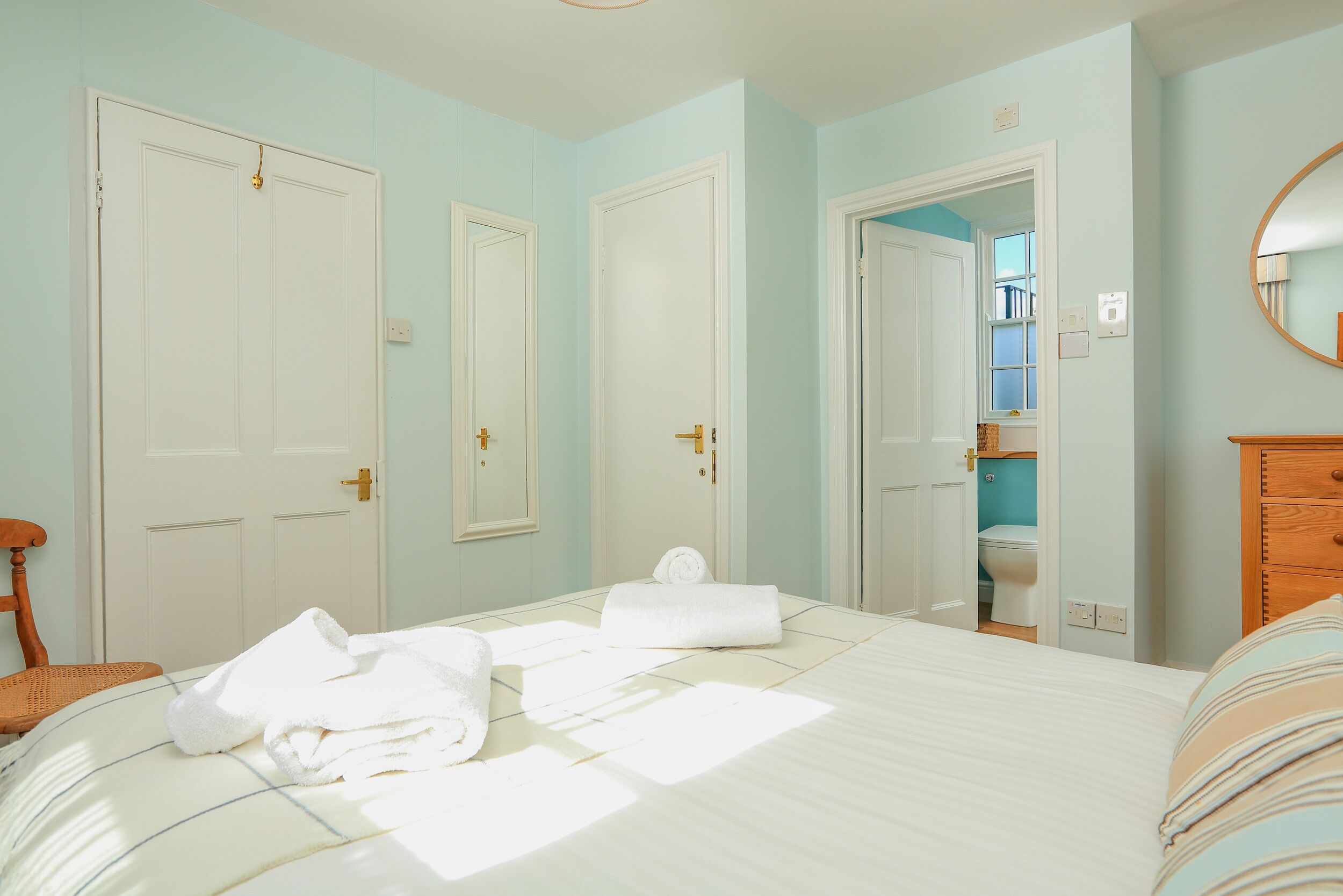 Una camera da letto con un letto, asciugamani bianchi, un comò in legno e un bagno visibile attraverso una porta aperta.