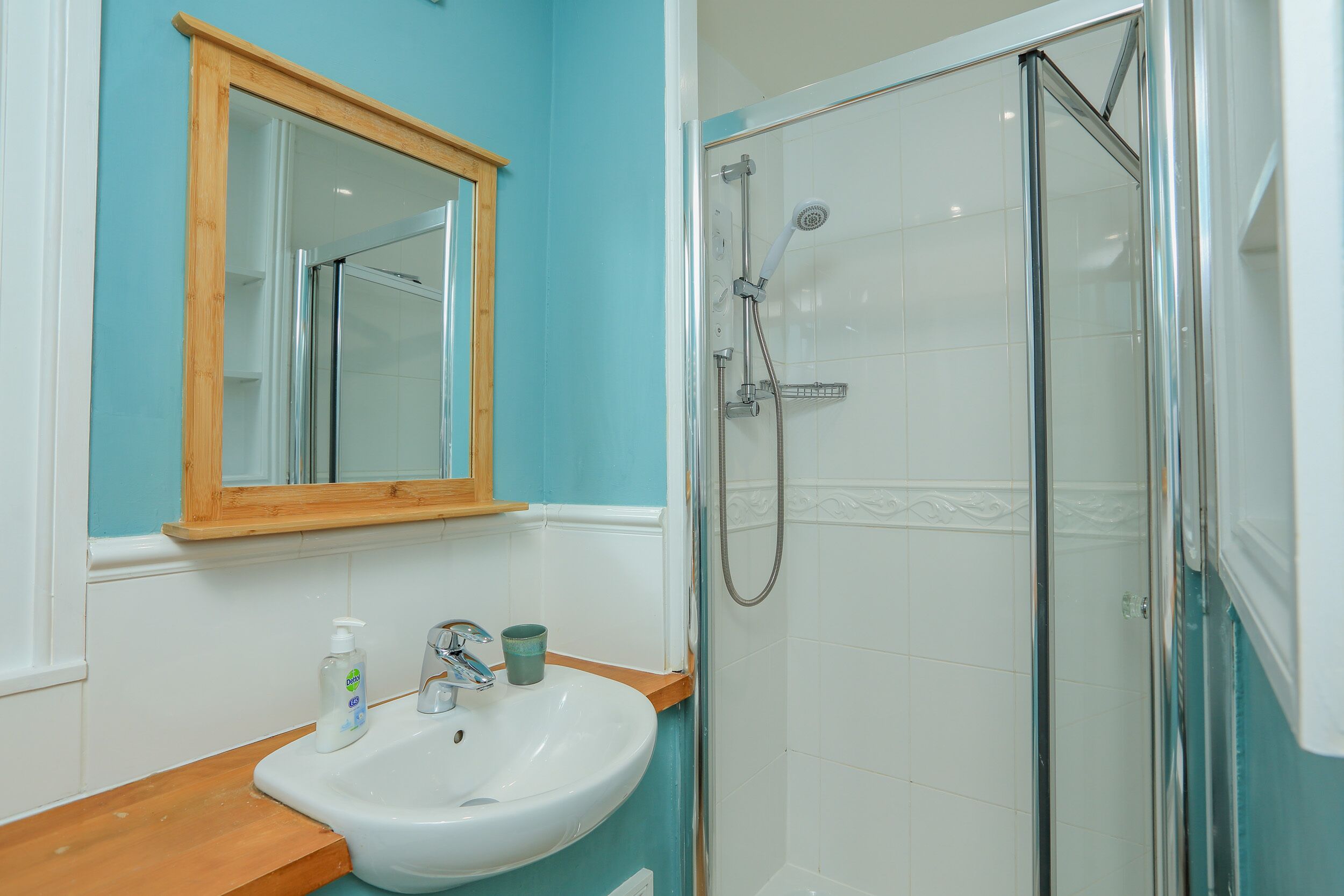A bathroom with a sink, mirror, and shower.