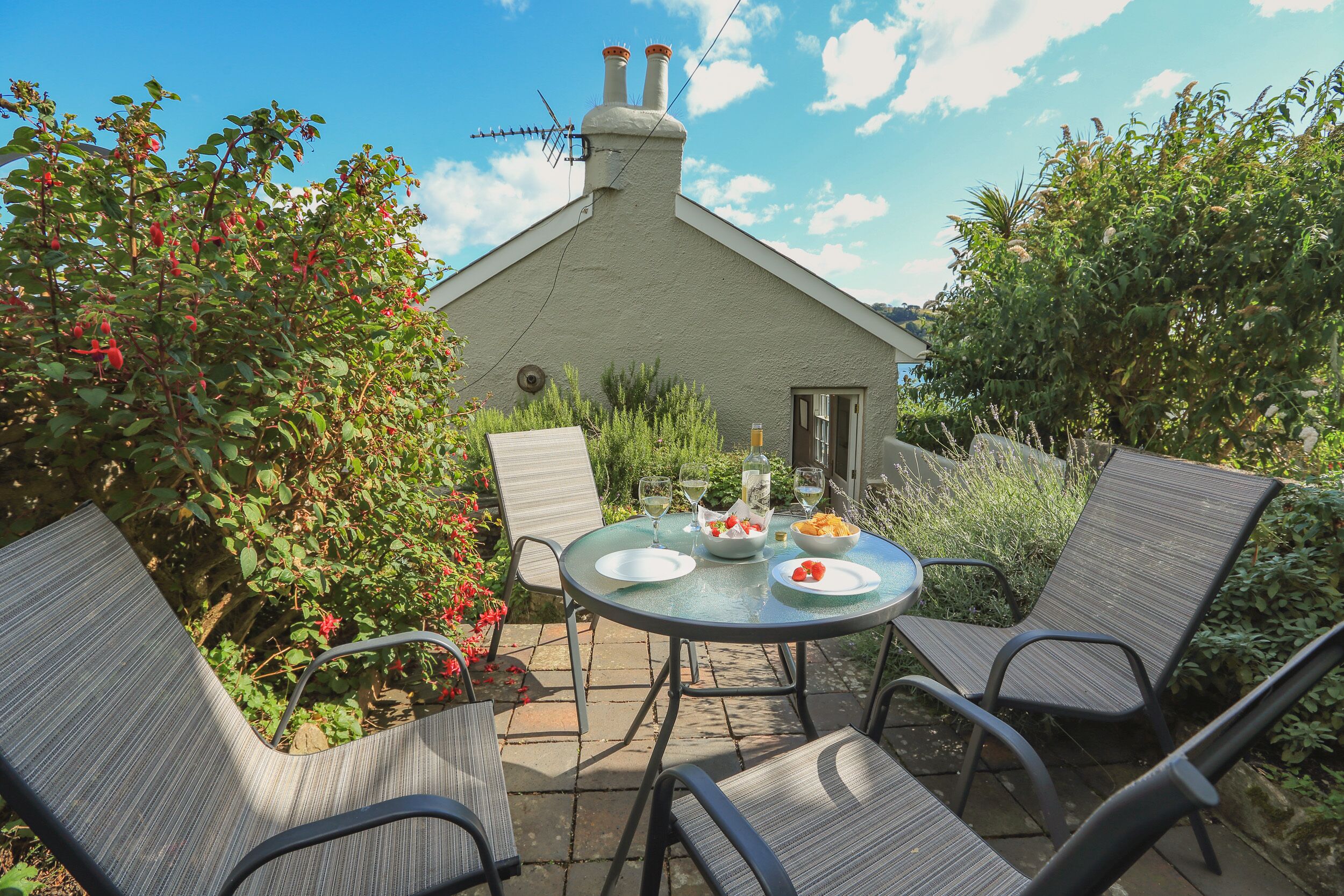 Eine Terrasse im Freien mit einem runden Tisch, vier Stühlen und einem kleinen Gebäude mit Schornstein.