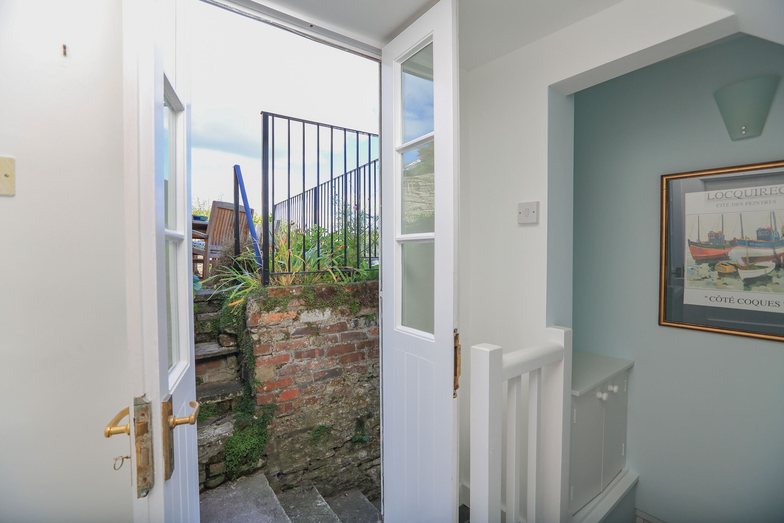 A narrow stairway leading to a balcony with a metal railing, a brick wall, and a door with a brass handle.