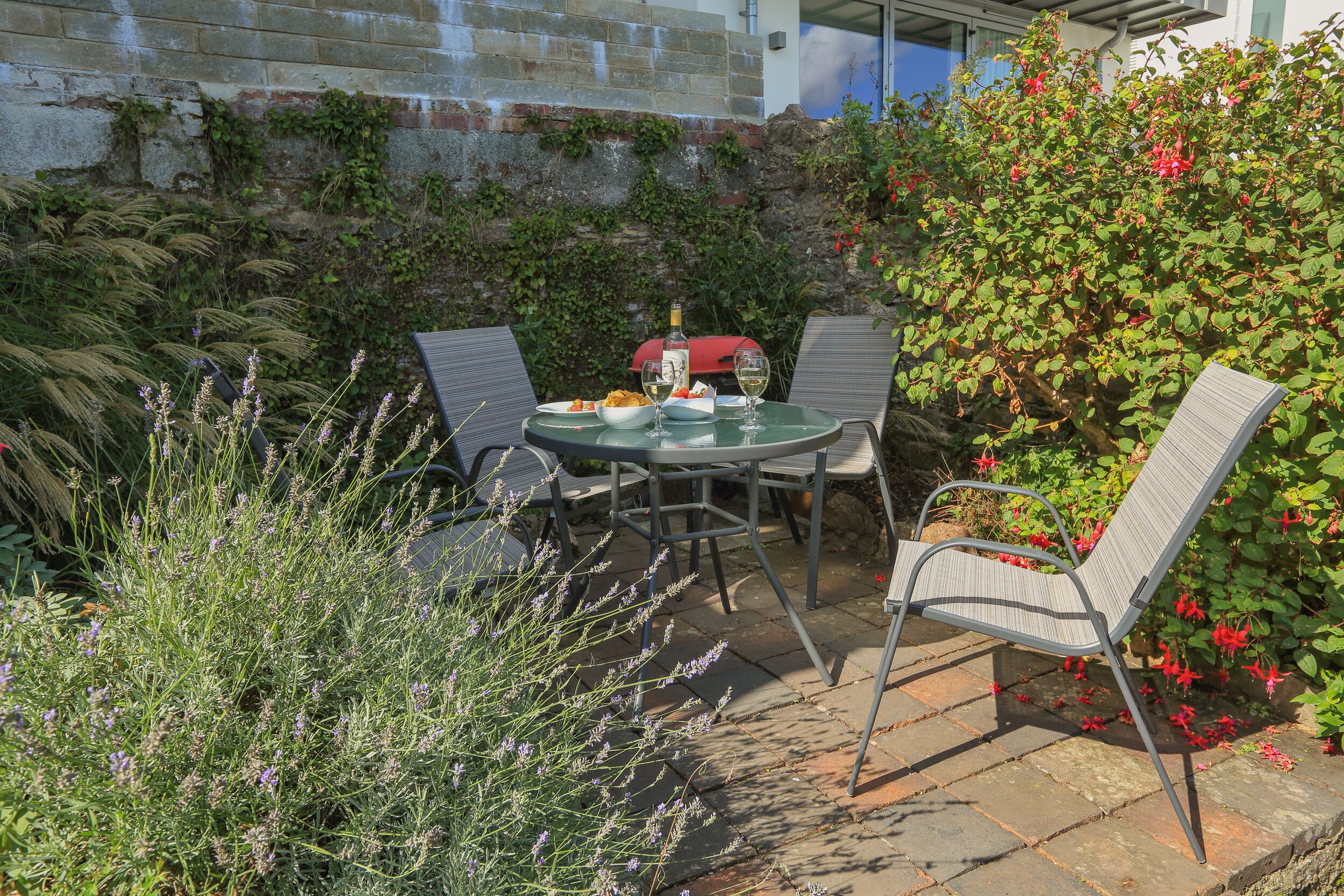 An outdoor patio with a round table, four chairs, and a red barbecue grill.
