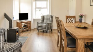 Un salon chaleureux avec une cheminée, un téléviseur, un fauteuil à carreaux et une table à manger avec des chaises.