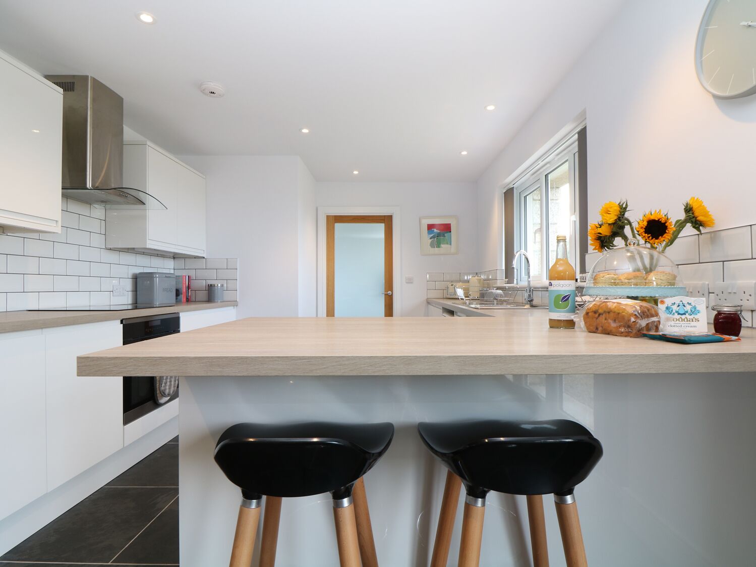 A modern kitchen with a central island, bar stools, and a window with sunflowers.