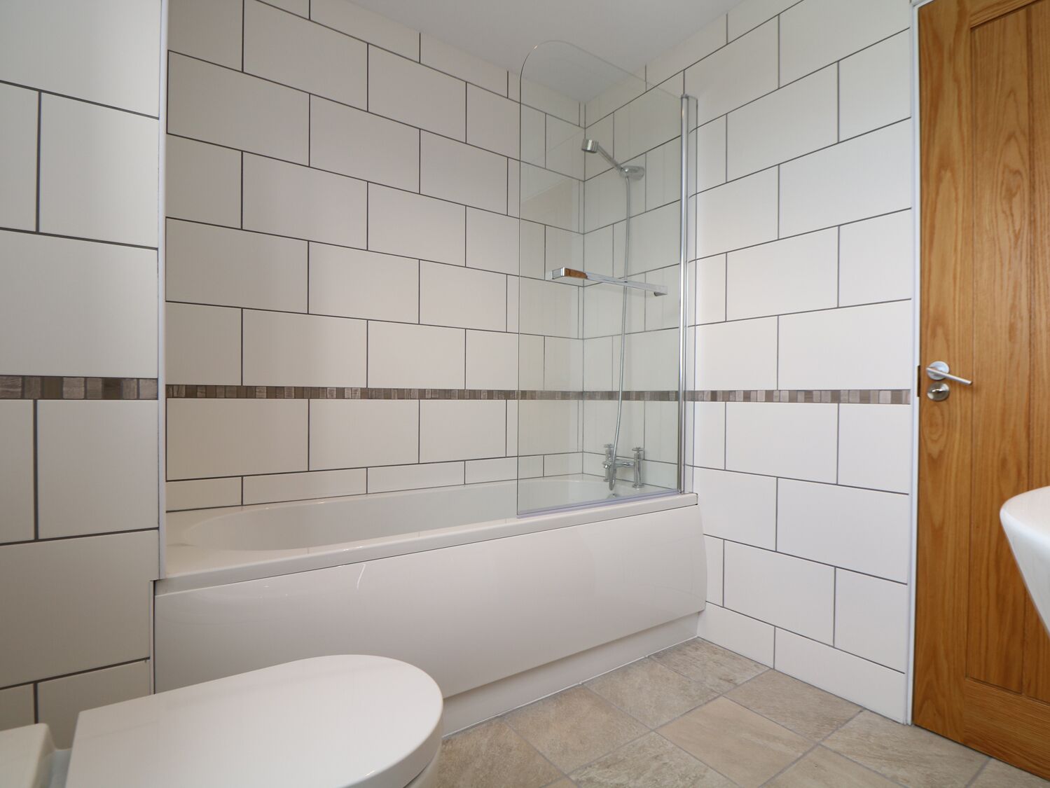 Um banheiro moderno com azulejos brancos, um chuveiro com divisória de vidro, uma banheira branca e uma porta de madeira.