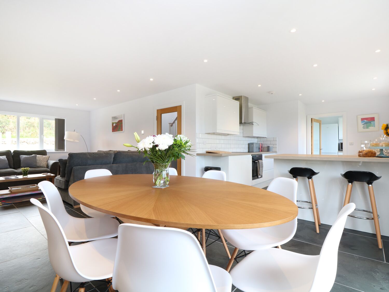 A modern kitchen with white cabinets, a wooden dining table, and white chairs.