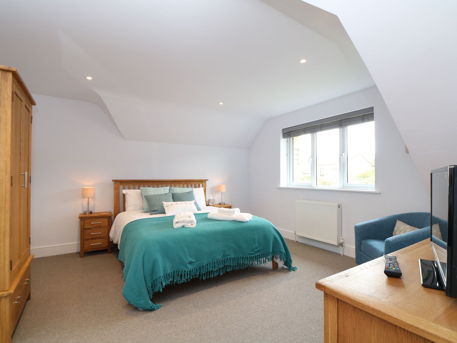 A bedroom with a bed, bedside tables, a TV, and a window.