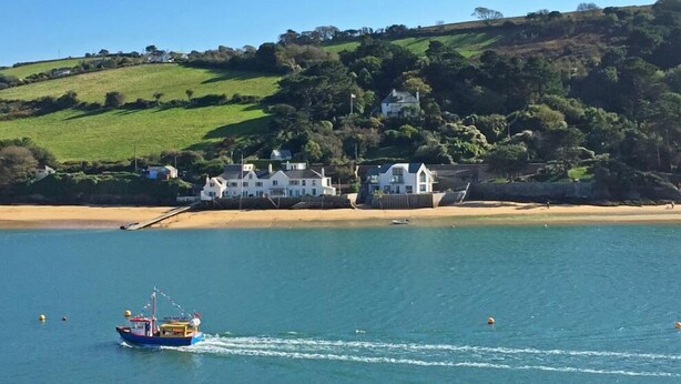 A coastal scene with a boat on the water, a sandy beach, and houses on a hillside. - Cloverwell (Kingsbridge)