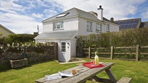 A house with a garden, a picnic table with a bottle and glasses, and a solar panel on the roof. - Cloverwell (Kingsbridge)