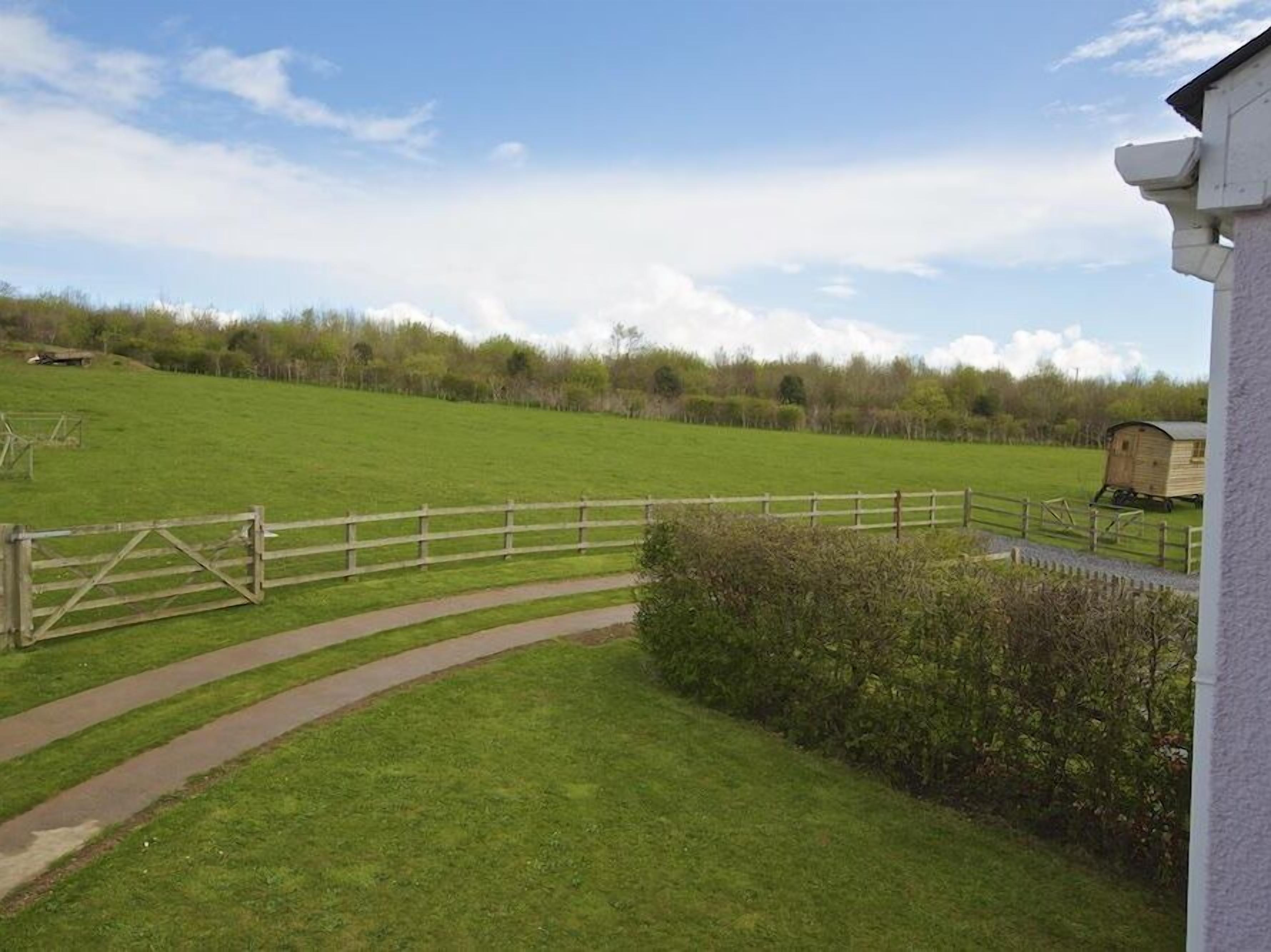 Een landelijk landschap met een grasveld, een houten omheining en een gebouw met een witte gevel.