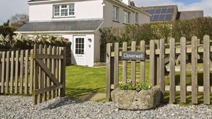 A two-story house with a white exterior, a black roof, and a solar panel on the roof. There is a wooden gate with a 'Cloverwell' sign in front. - Cloverwell (Kingsbridge)