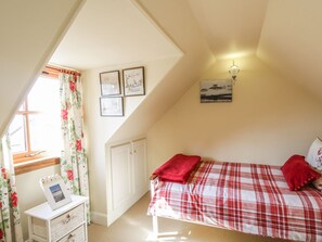 Ein Schlafzimmer mit Bett, Fenster mit Vorhängen, Nachttisch mit Foto und Wandbildern.