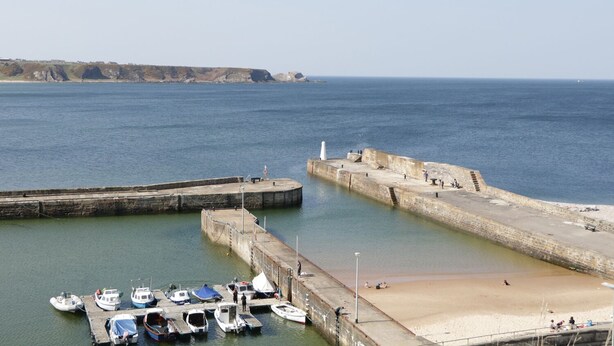 A coastal marina with boats docked, a sandy beach, and a lighthouse in the distance. - Sea Breeze Cottage (Buckie)