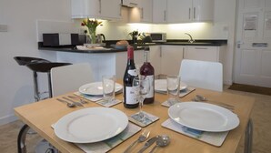 A dining area with a table set for two, a bottle of wine, and a clock on the wall. - Upper Fernlea (Salcombe)